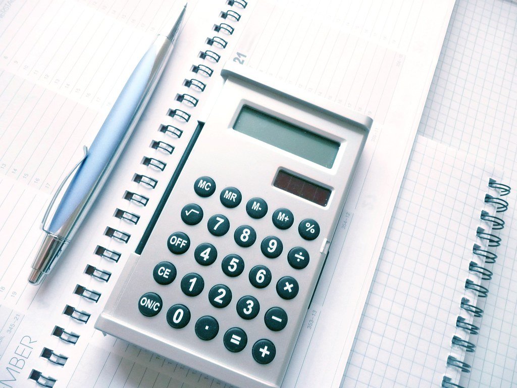 Calculadora, caneta e calendário sobre uma mesa representando o cálculo do 13º salário